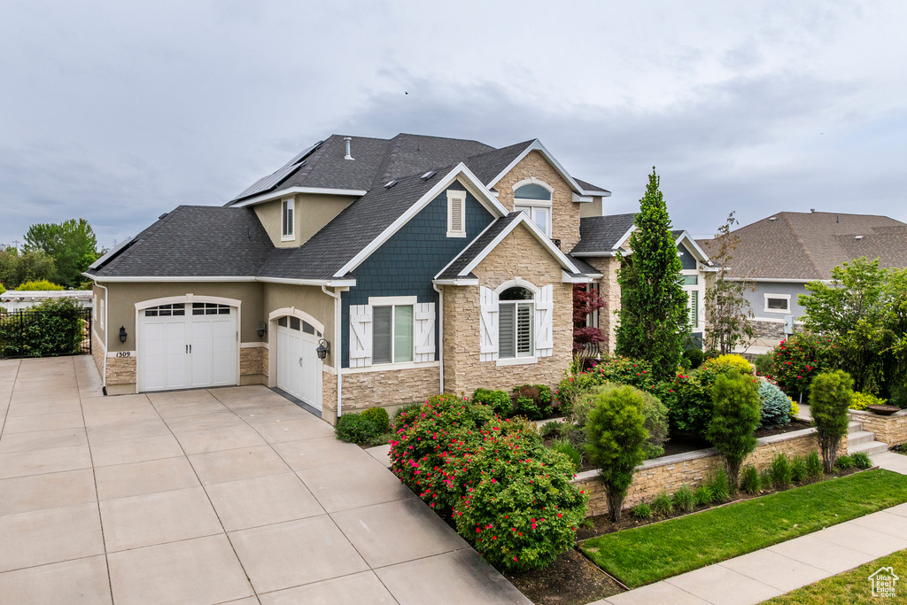 Craftsman-style house featuring stone siding, a garage, roof with shingles, and driveway