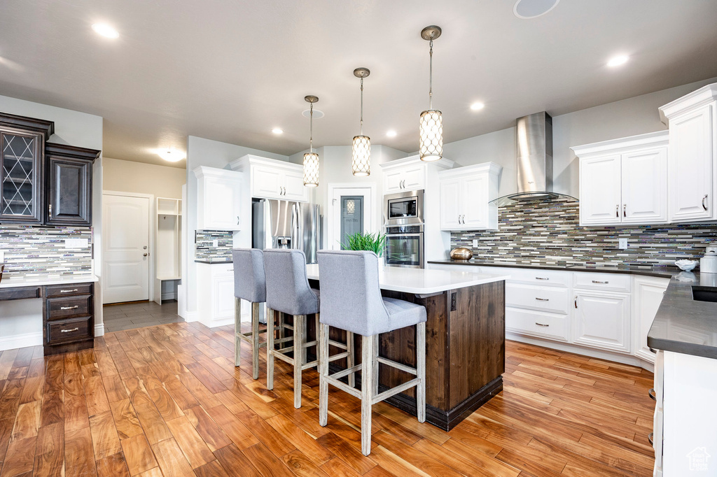 Kitchen with stainless steel appliances, wall chimney range hood, decorative backsplash, a center island, and white cabinetry