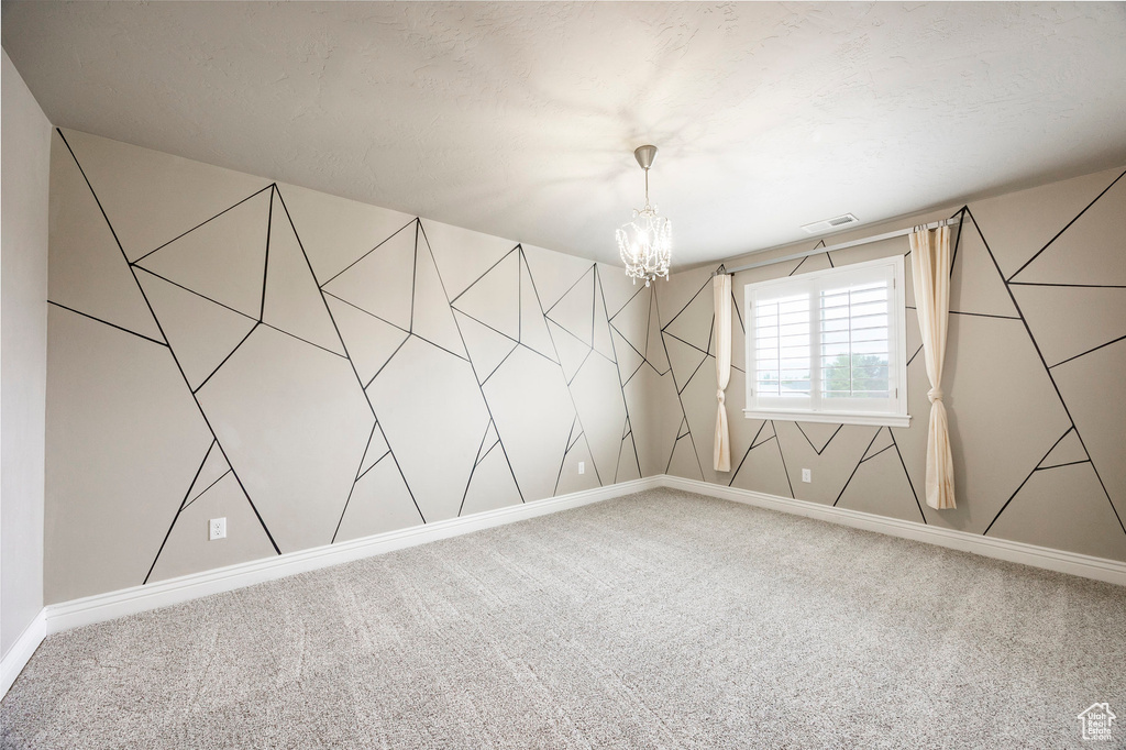 Carpeted spare room with a chandelier and baseboards