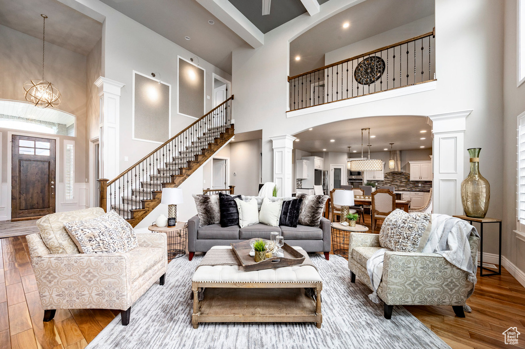 Living room featuring a towering ceiling, decorative columns, wood finished floors, stairs, and arched walkways