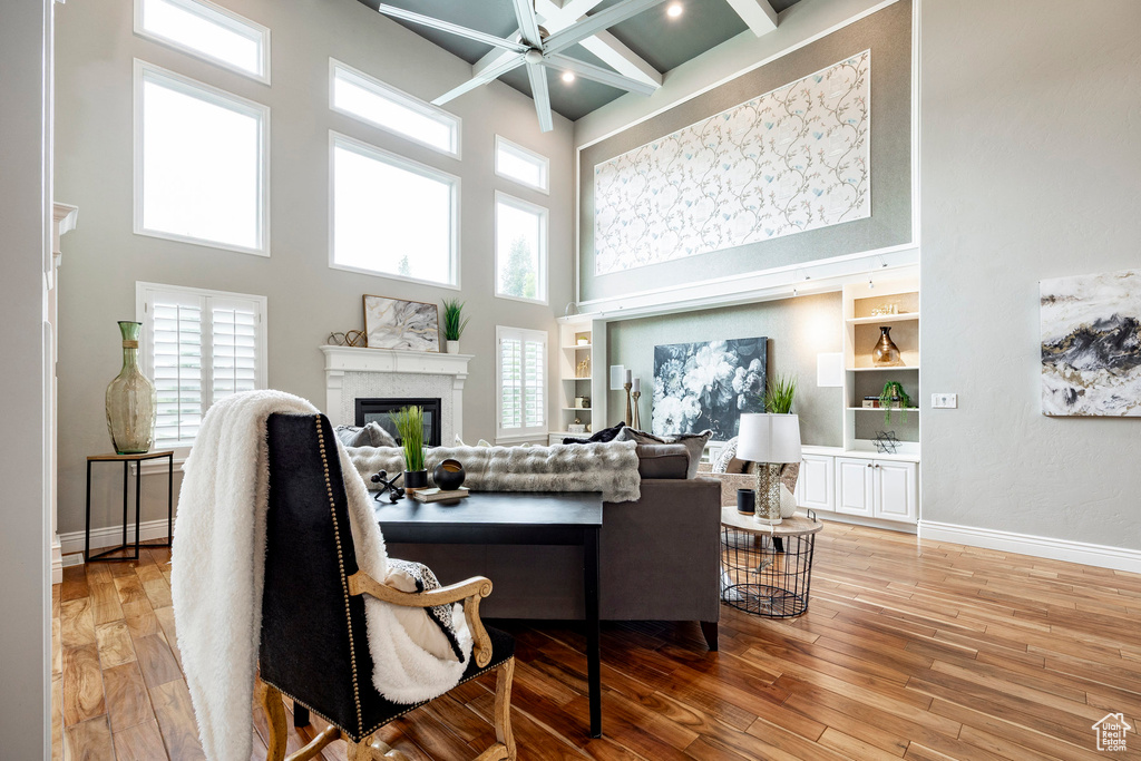 Living room with a high ceiling, a glass covered fireplace, light wood-type flooring, a ceiling fan, and baseboards