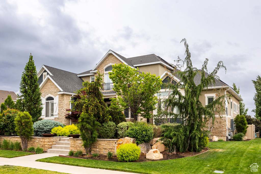 View of front of house featuring stone siding, a front yard, stucco siding, and roof with shingles