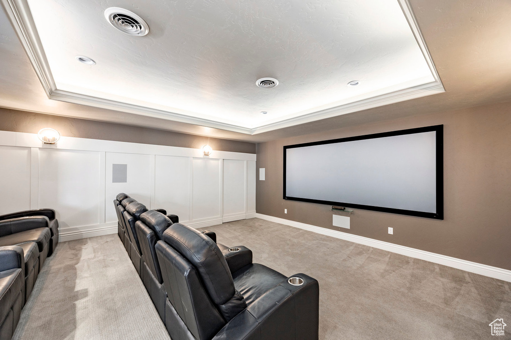 Home theater room with a raised ceiling, light carpet, and baseboards