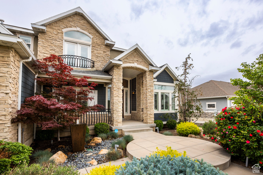View of front of property with a porch, stone siding, and a balcony