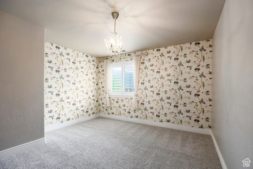 Carpeted spare room featuring wallpapered walls, a chandelier, and baseboards