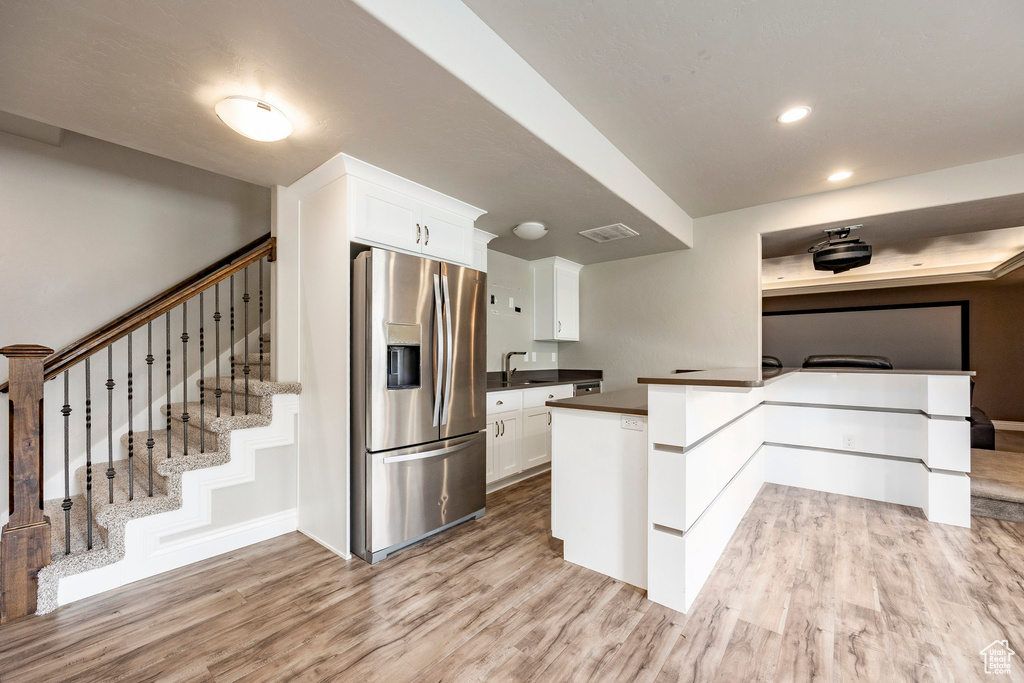 Kitchen featuring stainless steel fridge, dark countertops, light wood-style floors, white cabinets, and recessed lighting