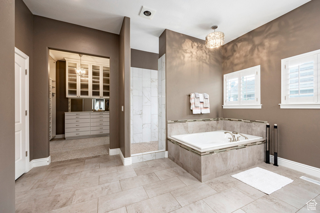 Bathroom with a tile shower, a bath, a chandelier, and baseboards