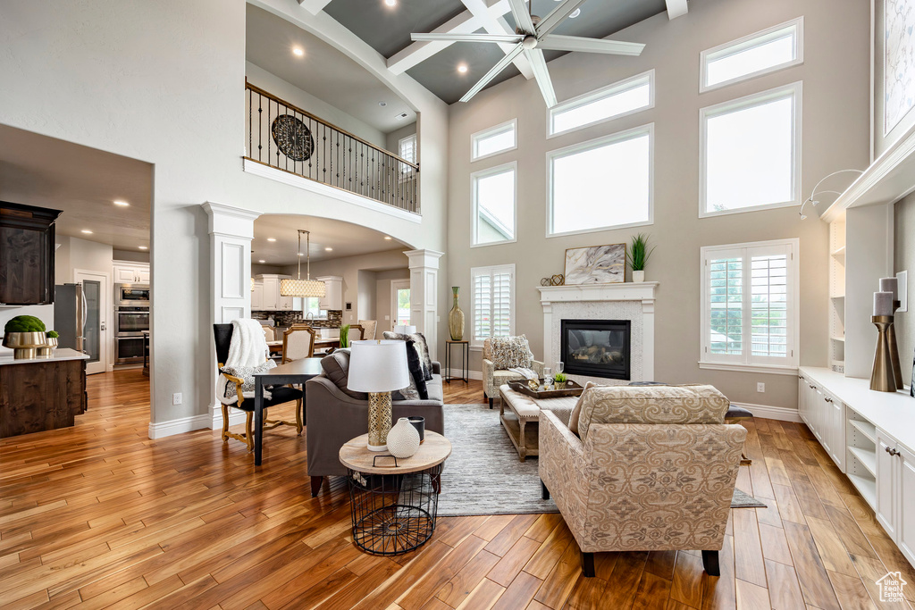 Living room featuring decorative columns, a towering ceiling, light wood-style flooring, a glass covered fireplace, and recessed lighting