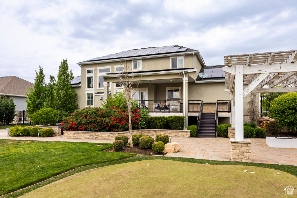 View of front of home featuring stucco siding, a putting area, roof mounted solar panels, a pergola, and stairs