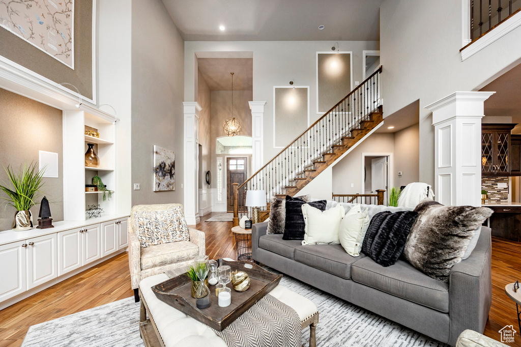 Living area featuring a high ceiling, light wood-style floors, stairs, ornate columns, and built in shelves
