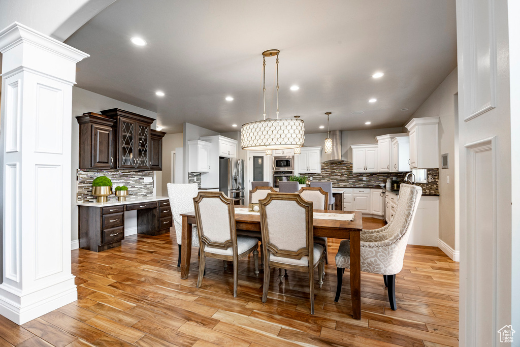 Dining area featuring light wood finished floors, decorative columns, recessed lighting, and arched walkways