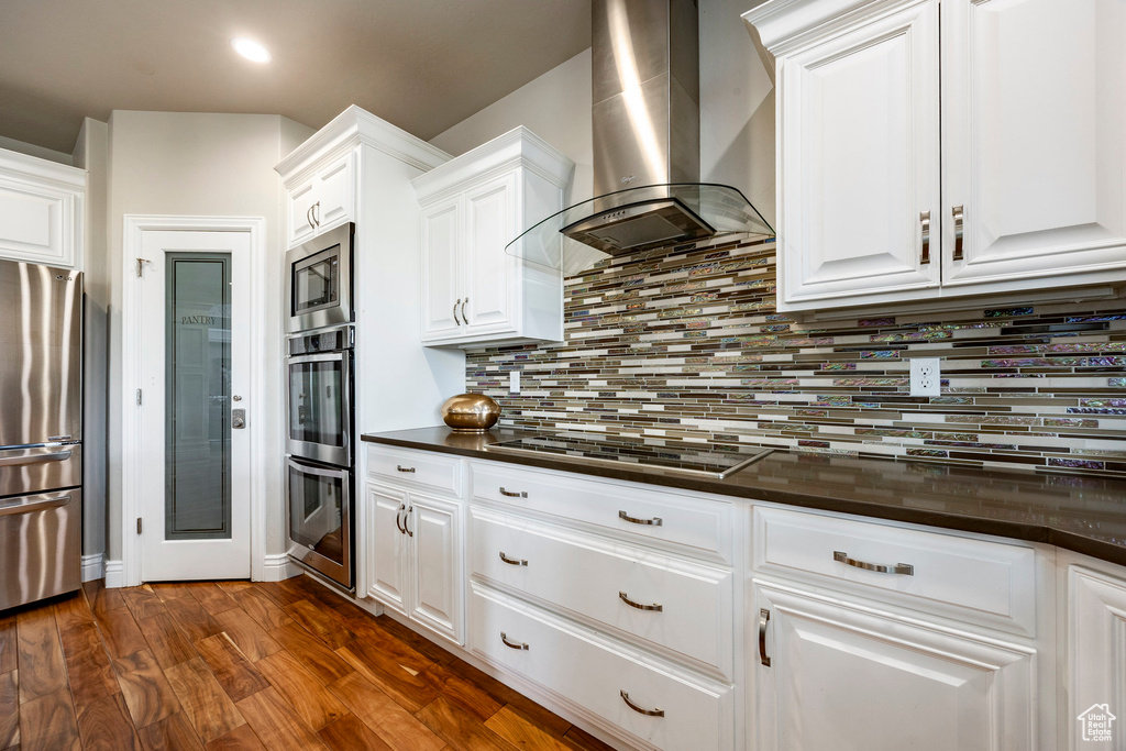Kitchen with wall chimney exhaust hood, appliances with stainless steel finishes, dark countertops, white cabinetry, and recessed lighting