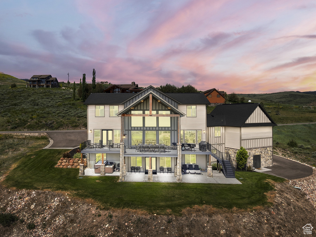 Back of property at dusk featuring a patio, stairs, a lawn, and driveway