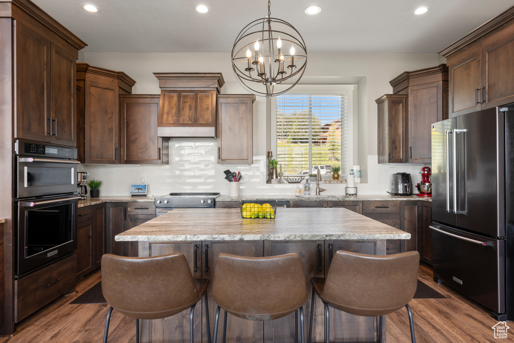 Kitchen with appliances with stainless steel finishes, a chandelier, a kitchen island, a breakfast bar, and recessed lighting