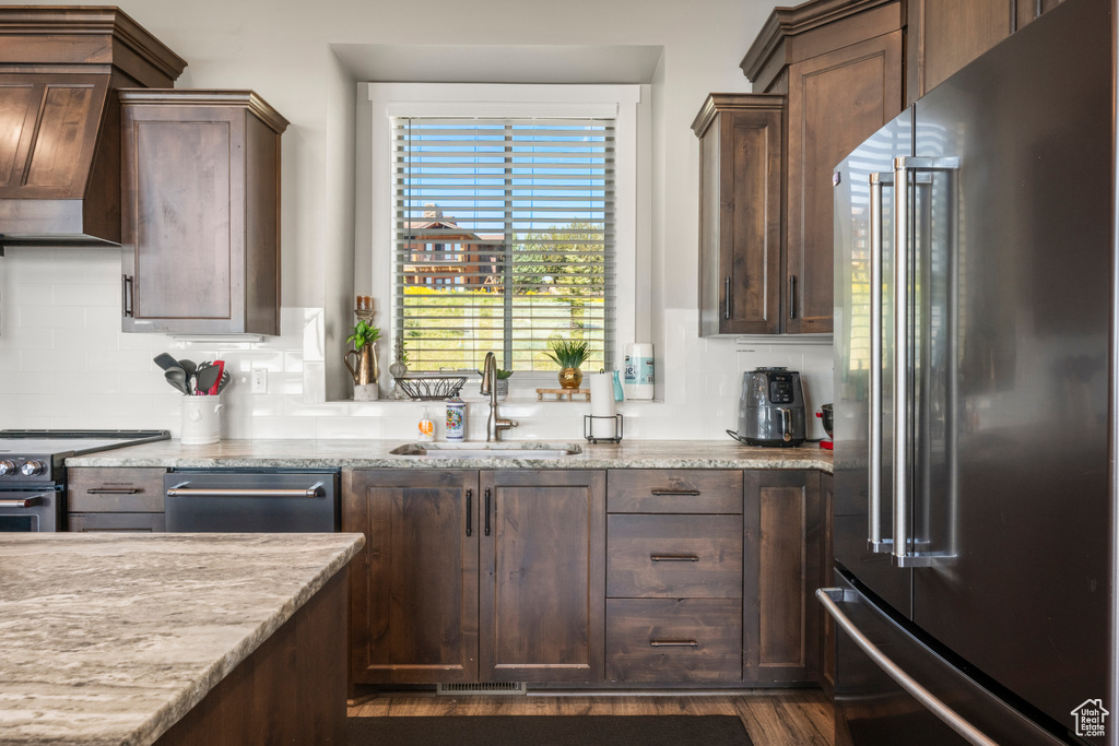 Kitchen with stainless steel appliances, custom range hood, light stone countertops, tasteful backsplash, and dark wood-type flooring