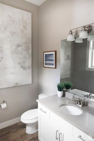 Bathroom featuring toilet, wood finished floors, vanity, and baseboards