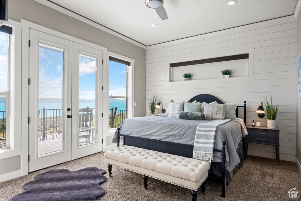 Bedroom featuring carpet flooring, access to outside, crown molding, a water view, and wooden walls