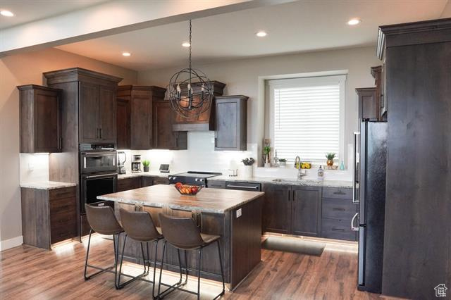 Kitchen featuring a sink, freestanding refrigerator, a center island, wood finished floors, and recessed lighting
