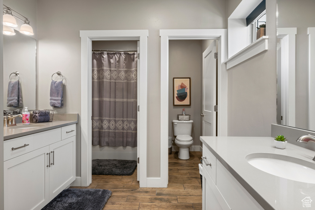 Full bath with wood finished floors, two vanities, and a shower with curtain