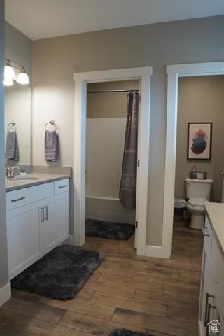 Full bathroom featuring wood finished floors, vanity, a shower with shower curtain, toilet, and baseboards