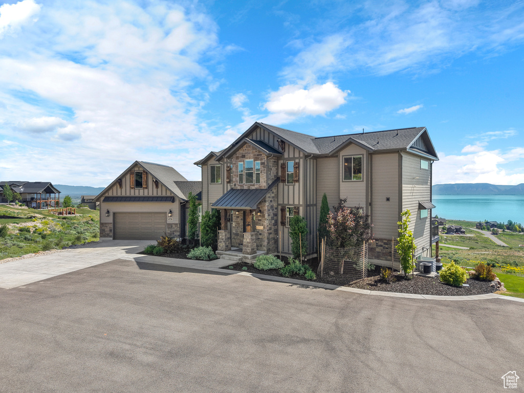 View of front of house featuring board and batten siding, stone siding, driveway, and a water view