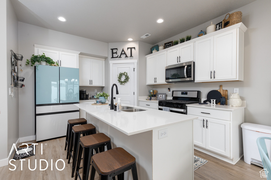 Kitchen with stainless steel appliances, a sink, light wood-type flooring, white cabinetry, and recessed lighting