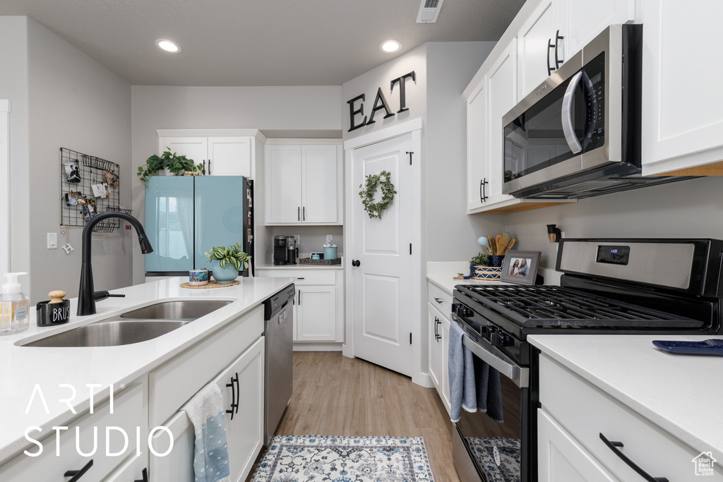 Kitchen with stainless steel appliances, a sink, light wood-style floors, light countertops, and white cabinets