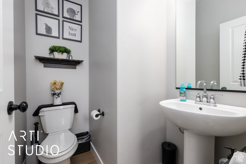 Half bathroom with toilet, a sink, wood finished floors, and baseboards