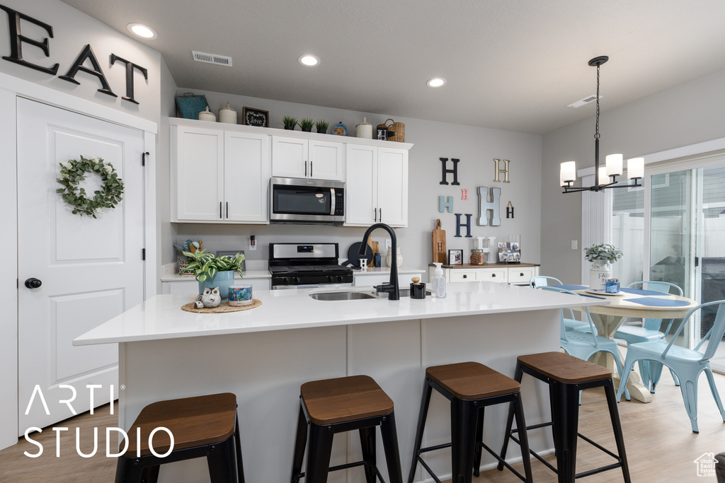 Kitchen featuring stainless steel appliances, a sink, white cabinets, a chandelier, and light wood finished floors