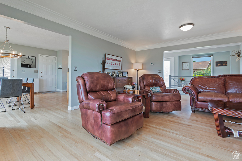 Living room with light wood-style floors, a chandelier, crown molding, and baseboards