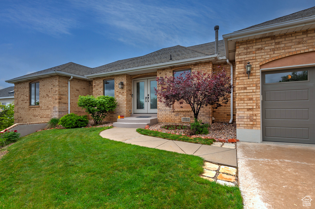 View of front facade with french doors, brick siding, a front lawn, a garage, and roof with shingles