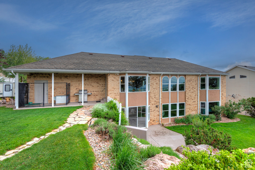 Back of house featuring a lawn, brick siding, a patio, and roof with shingles