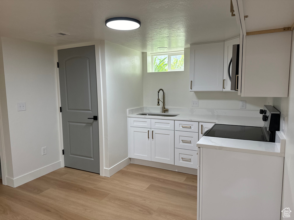 Kitchen with black range with electric stovetop, a sink, light wood-style flooring, white cabinetry, and light countertops