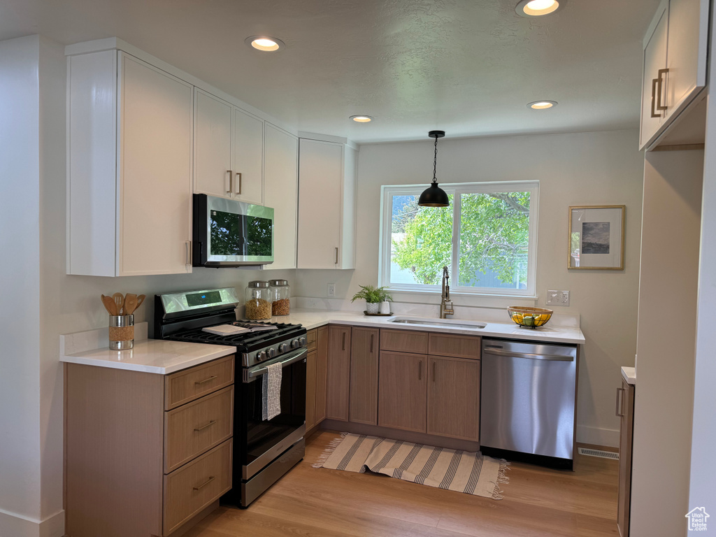 Kitchen with stainless steel appliances, a sink, light wood finished floors, light countertops, and recessed lighting