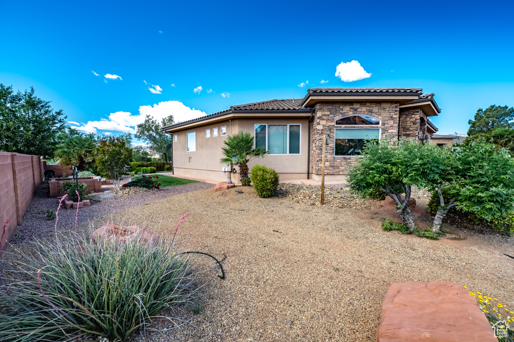 View of front of property featuring a tile roof, stone siding, fence, and stucco siding
