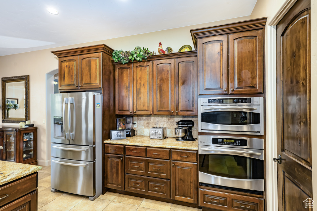 Kitchen featuring stainless steel appliances, light tile patterned floors, light stone counters, and tasteful backsplash