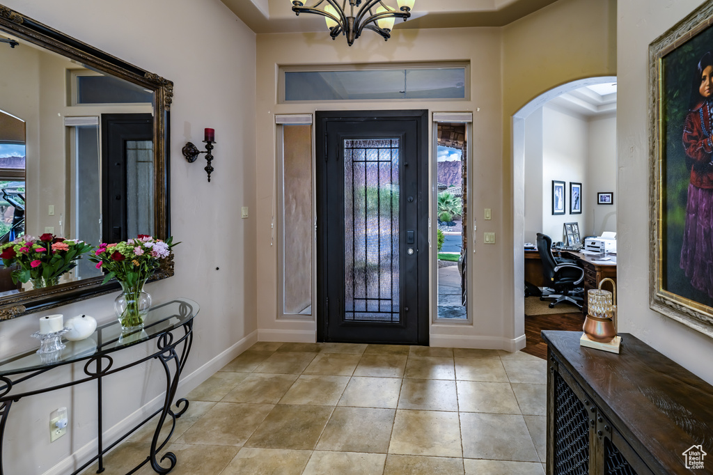 Entryway with arched walkways, healthy amount of natural light, light tile patterned floors, and a chandelier