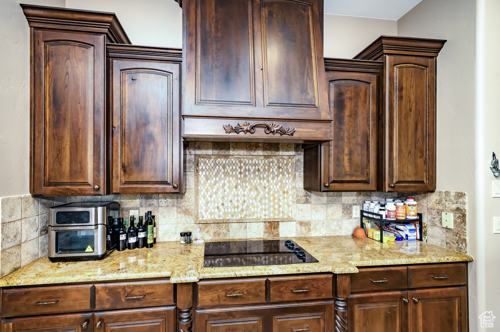 Kitchen featuring black electric cooktop, backsplash, light stone counters, and dark brown cabinetry