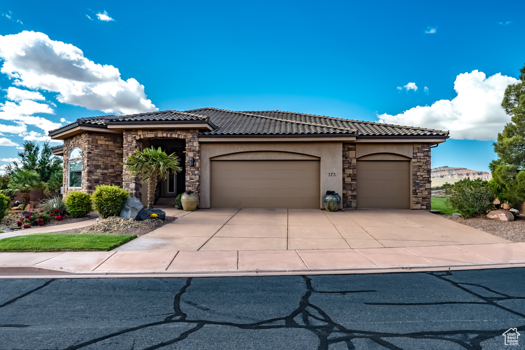 View of front of home featuring stone siding, an attached garage, a tile roof, and stucco siding
