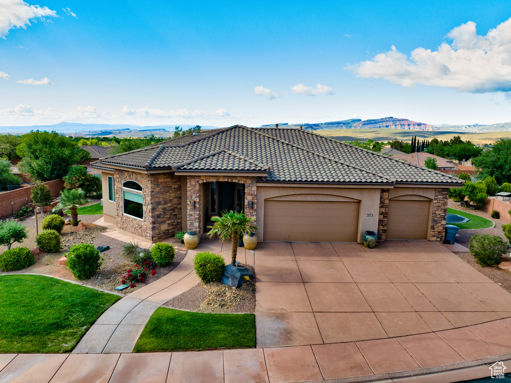 Mediterranean / spanish house with stucco siding, an attached garage, a mountain view, and stone siding