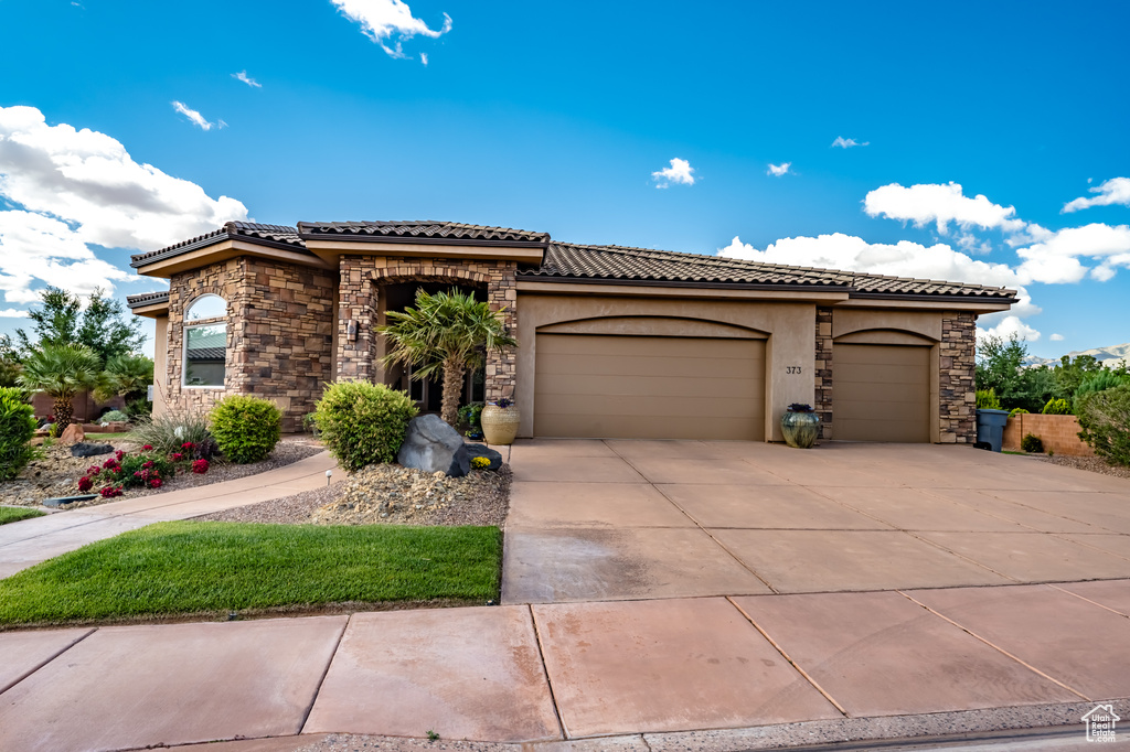 Mediterranean / spanish-style home featuring a tiled roof, a garage, driveway, stucco siding, and stone siding