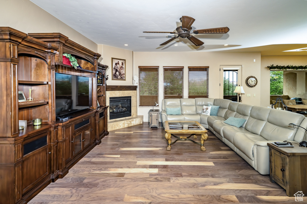 Living area with ceiling fan, a glass covered fireplace, wood finished floors, and recessed lighting
