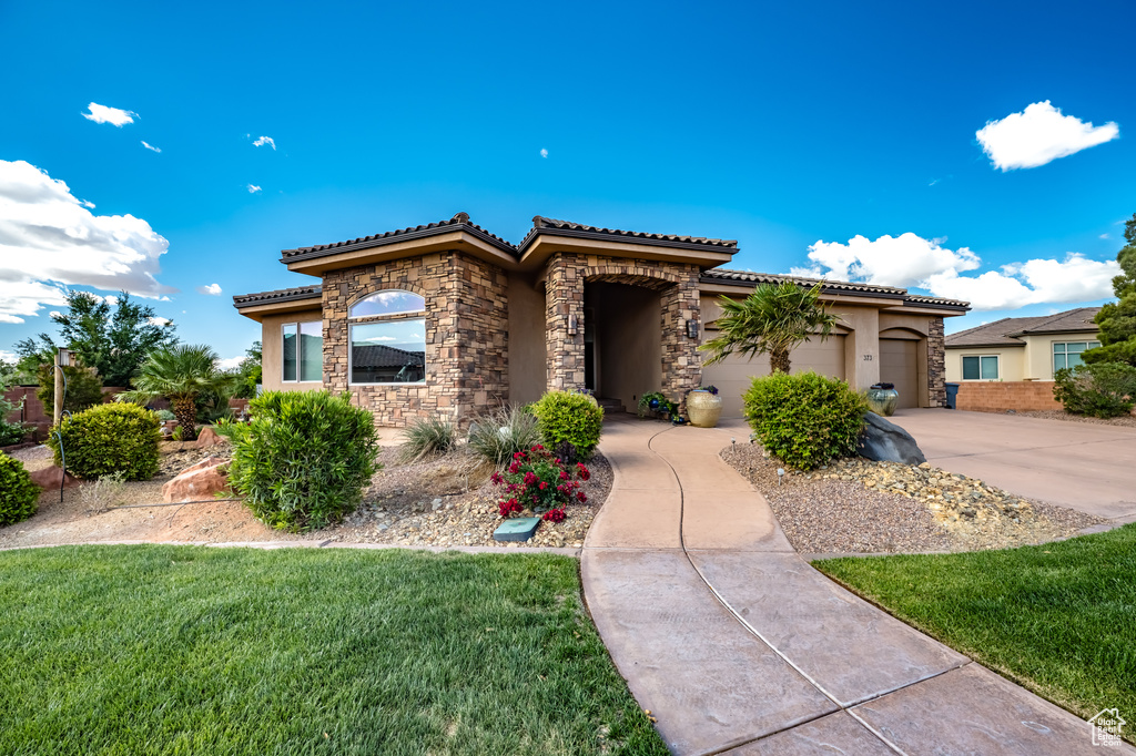 Mediterranean / spanish house with stone siding, stucco siding, a tile roof, concrete driveway, and a garage