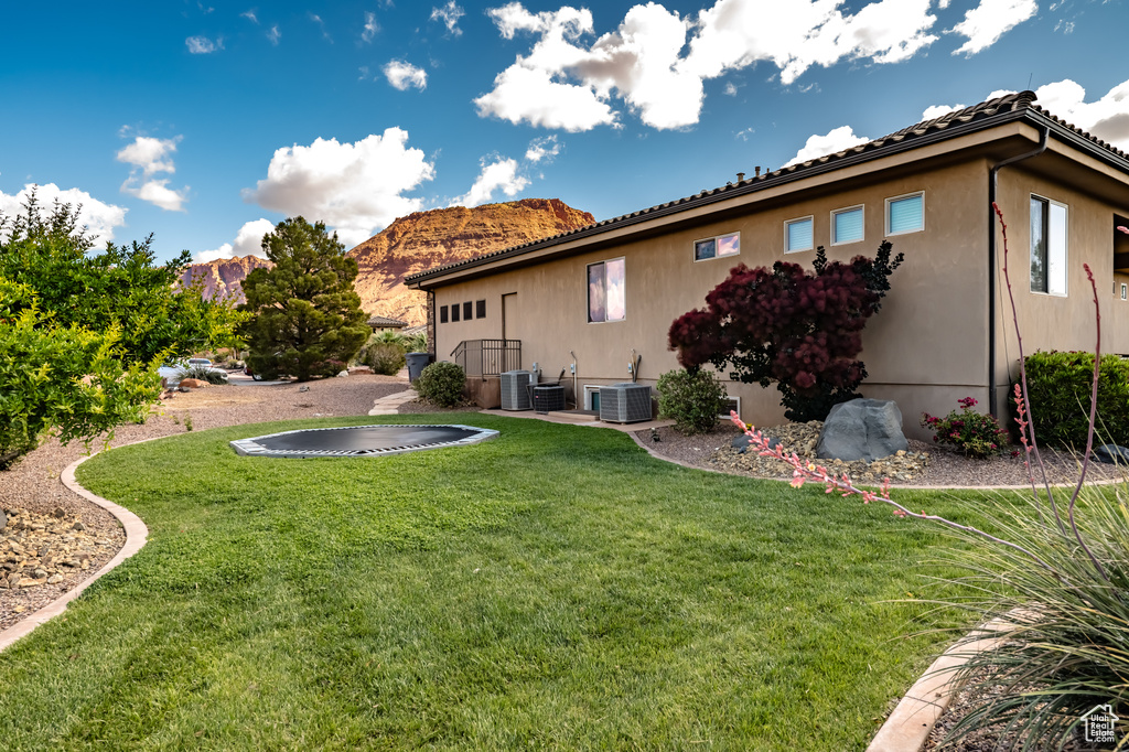 Back of house with central AC unit, a lawn, a mountain view, and stucco siding