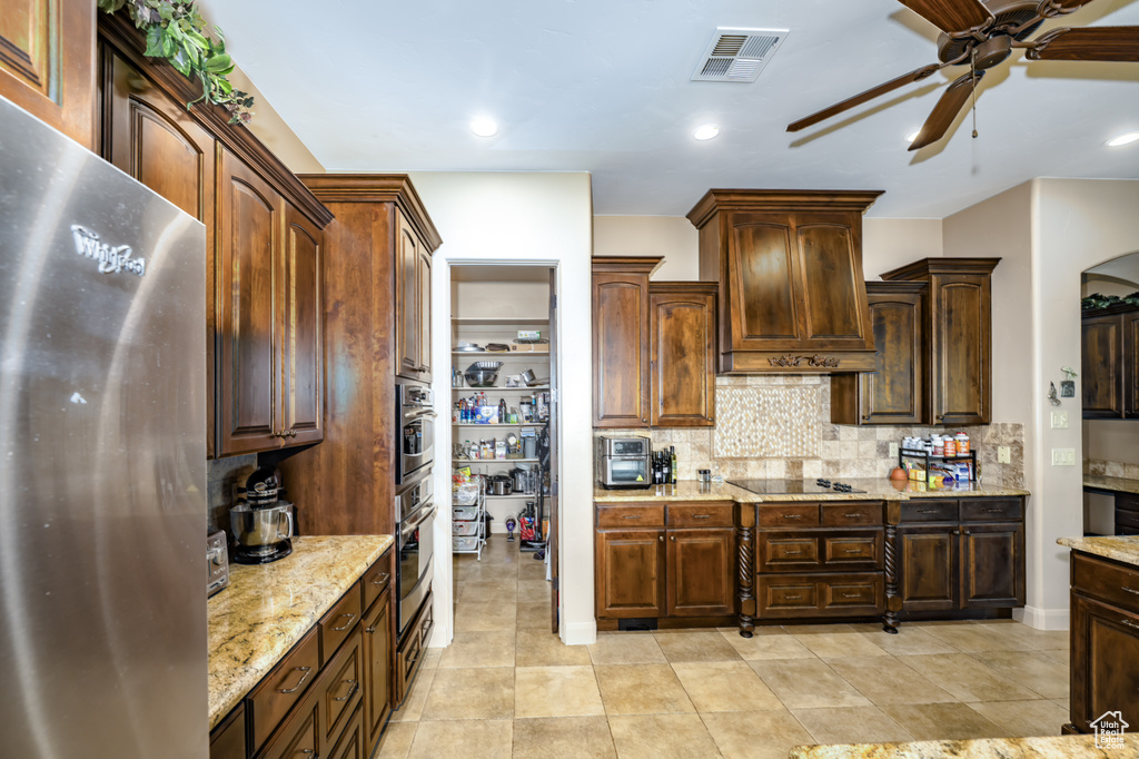 Kitchen featuring stainless steel appliances, a ceiling fan, tasteful backsplash, light stone countertops, and arched walkways