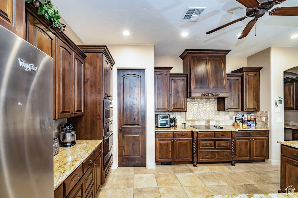 Kitchen with stainless steel appliances, a ceiling fan, backsplash, custom exhaust hood, and light stone counters
