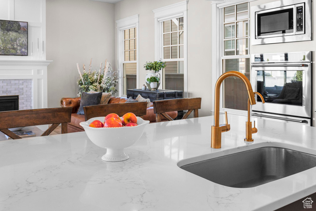 Detailed view of appliances with stainless steel finishes, a sink, a fireplace, and light stone counters