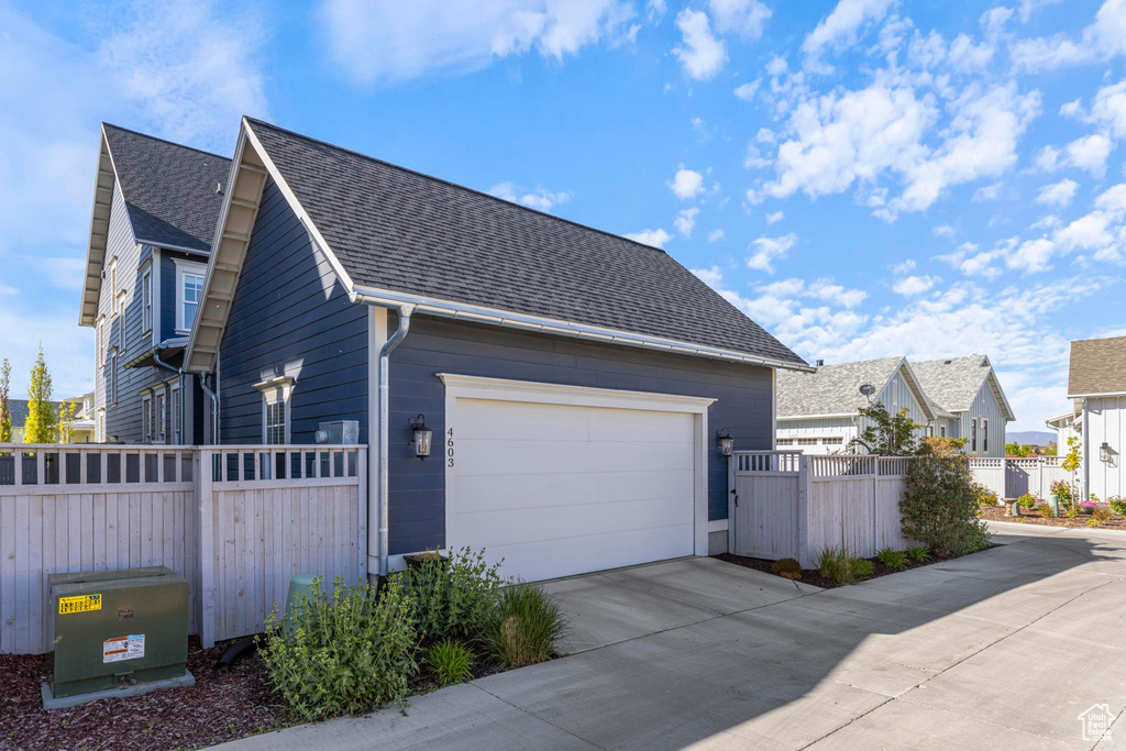 View of side of home with a shingled roof, fence, and driveway