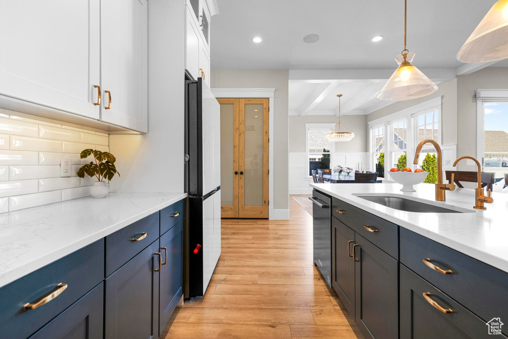 Kitchen featuring a sink, light wood-style flooring, white cabinetry, freestanding refrigerator, and hanging light fixtures