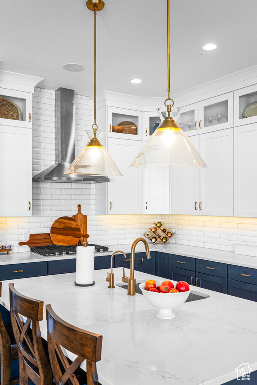 Kitchen with wall chimney exhaust hood, hanging light fixtures, white cabinetry, and recessed lighting